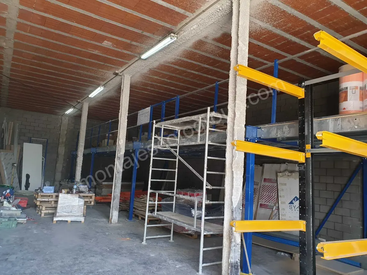 Estructura de entreplanta junto a una torre de andamio y brazos amarillos de una estantería cantilever en una nave
